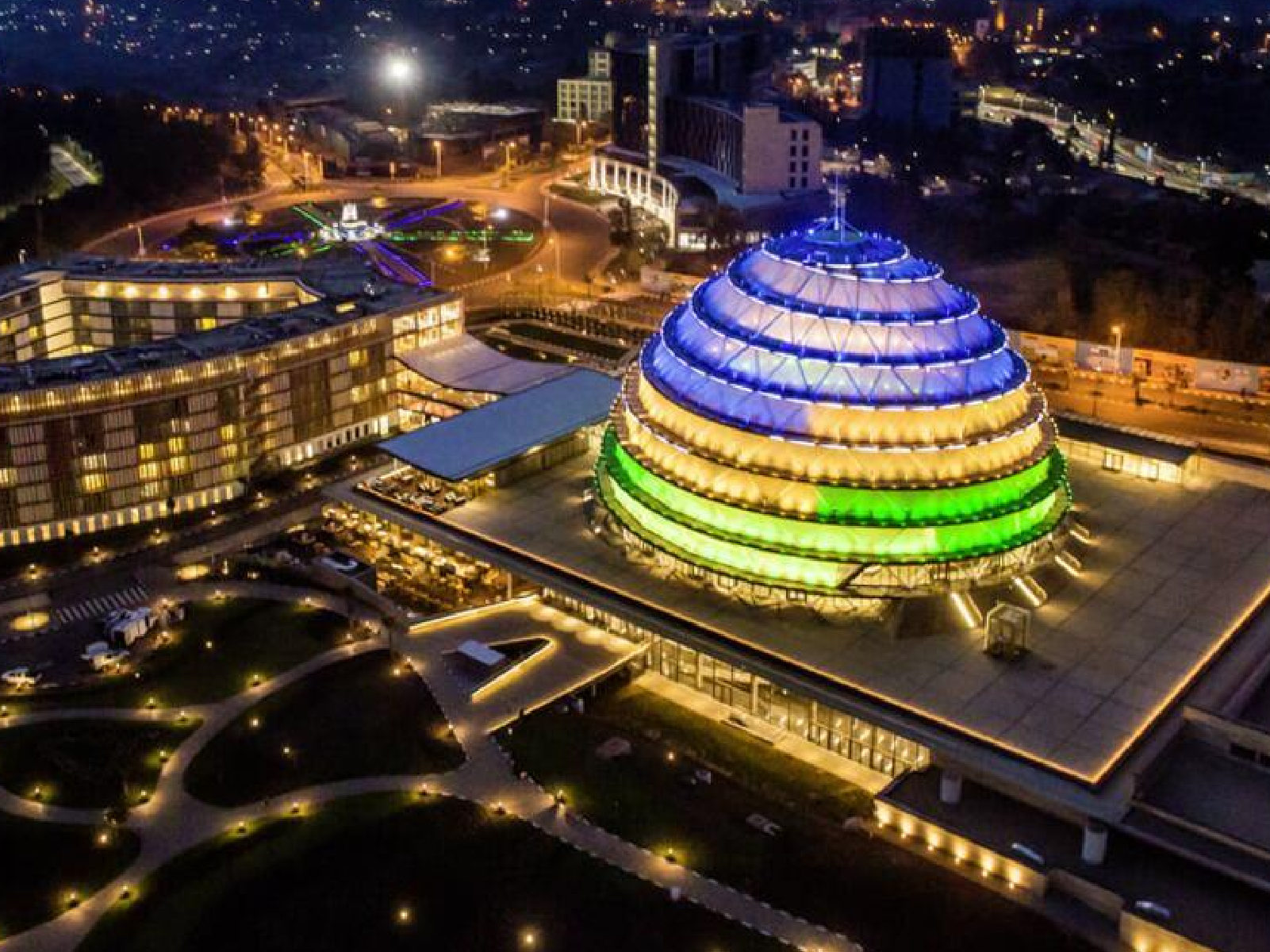 Kigali Convention Centre dome lit in blue, yellow and green at night.